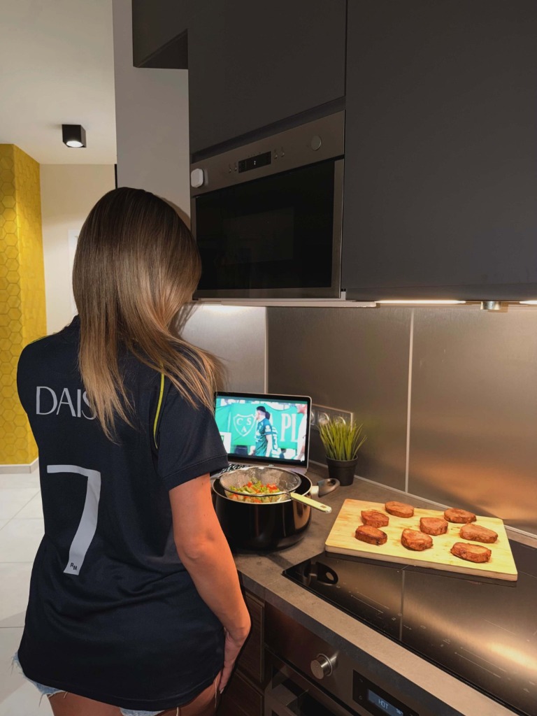 Daisy a 7-es mezében a konyhában főzés közben meccset néz a laptopon